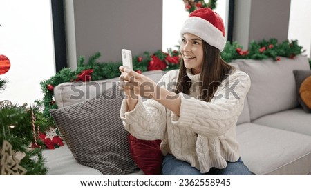 Young beautiful hispanic woman make photo by smartphone to christmas tree at home