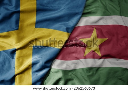 big waving national colorful flag of sweden and national flag of suriname . macro