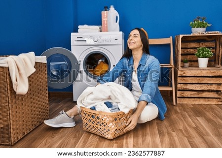 Young beautiful hispanic woman smiling confident washing clothes at laundry room