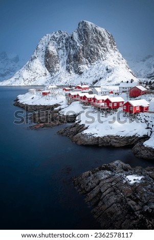 Vertical photo of Hamnoy fishing village in Norway. Lofoten winter scene with typical red houses and a snowy mountain in the background.
