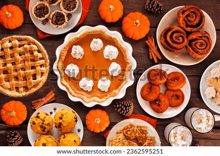 Autumn desserts table scene with an assortment of traditional fall sweet treats. Above view over a rustic wood background. Pumpkin and apple pies, apple cider donuts, muffins, cookies, tarts. Royalty-Free Stock Photo #2362595251