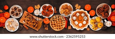 Autumn desserts table scene with a variety of traditional fall sweet treats. Top down view over a rustic wood banner background. Pumpkin and apple pies, apple cider donuts, muffins, cookies, tarts. Royalty-Free Stock Photo #2362595253