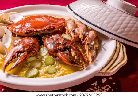 stewed mixed seafood platter crab, shell clam, tiger prawn in hot clay pot with rice and yellow chicken stock congee on red cloth table tea pot asian Chinese halal food restaurant banquet cuisine menu