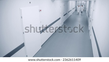 Bright clinic corridor: Female doctor and elderly woman walk down the hallway to hospital ward, talk about treatment. Medical staff work in modern medical facility. Security camera view. High angle. Royalty-Free Stock Photo #2362611409