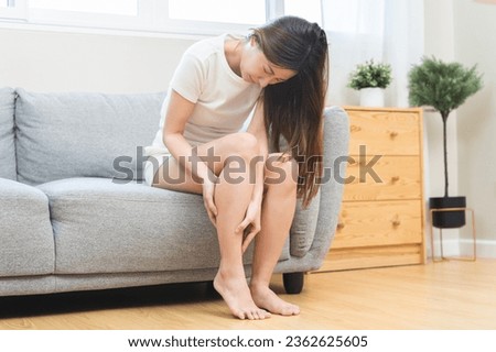 Muscle pain or leg pain, suffer asian young woman, girl hand massaging brawn leg calf muscle cramps or spasm, trauma from inflammation of tendon at calves while sitting on sofa. Health care concept. Royalty-Free Stock Photo #2362625605