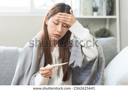 Sick, influenza asian young woman, girl have a fever, hand holding thermometer, touching forehead for check measure body temperature, illness while lying rest on sofa at home. Health care concept. Royalty-Free Stock Photo #2362625641