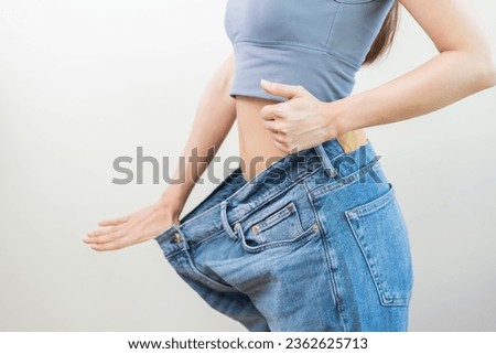 Shape slender, thin waist, attractive slim asian young woman hand show thumb and shape her weight loss, wearing in big, large or oversize jeans, excess lose by diet and exercise, body fit healthy. Royalty-Free Stock Photo #2362625713