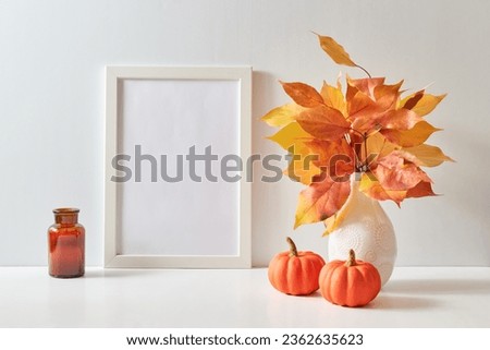 Mockup with a white frame and colorful autumn leaves in a vase on a light background. Empty poster frame mockup for presentation design, text, lettering
