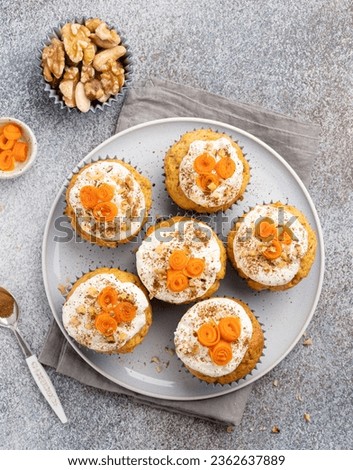 Carrot (pumpkin) cupcakes with swirls of sliced carrot, chopped nuts, cream and cinnamon powder. Festive autumn baking. Seasonal cooking. TCloseup view. Decorated vegetable muffins on plate.  Royalty-Free Stock Photo #2362637889