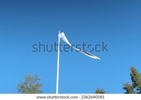 Finnish pennant on a flagpole in countryside in Finland. Blue sky, trees in the background, sunny windy autumn day, no people, sign of landowners being home, old pennant tradition