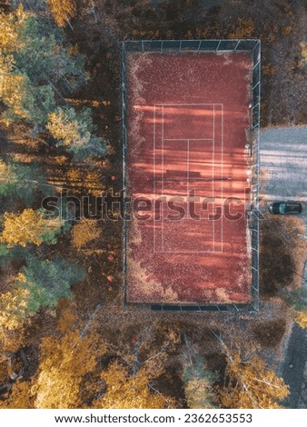 Aerial view of tennis court. Moody autumn weather lots of fallen leaves on the court. A car parked beside court.
