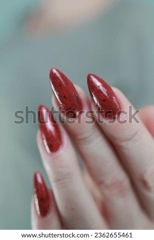 Female hand with long nails and a red marsala manicure holds a bottle of nail polish