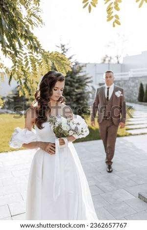 An adult groom in a brown suit walks to the bride. The bride in a chic dress in the foreground. Outdoor wedding in sunset light, wedding, marriage, relationship, lifestyle