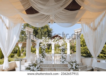 the wedding ceremony is decorated with fresh flowers on the location with tall white columns. Preparation for the wedding ceremony