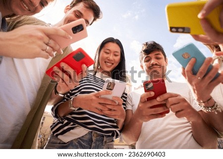 Low angle view multiracial group young generation z in circle using phones together outdoors. Cheerful student friends looking at mobile enjoying social media content. People and technology addiction  Royalty-Free Stock Photo #2362690403