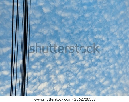 a landscape photograph of a blue sky with small clouds and a black power line extending upwards on the left of the image.
