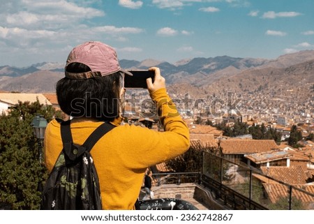 Tourist with cell phone in hand taking pictures of the city of Cusco from the San Blas viewpoint in the Peruvian Andes.