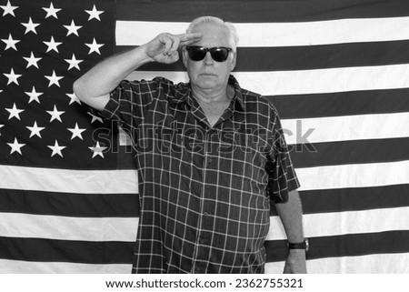Photo Booth. American Flag. A proud American Man Salutes and Poses in front of the American Flag while waiting for his pictures to be taken while in a photo booth at a Fourth of July Party. America. 