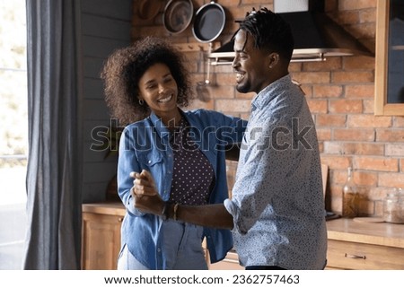 Happy loving African American couple holding hands, dancing in kitchen at home together, smiling beautiful wife and husband moving to favorite music, enjoying romantic date, celebrating relocation Royalty-Free Stock Photo #2362757463