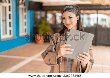 Young pretty woman holding a tablet at outdoors with happy expression