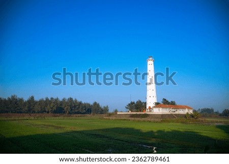 White lighthouse with green meadow on foreground and clear blue sky - Ketawang Beach, Indonesia