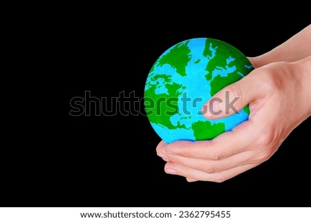 Cupped hands extend a verdant globe from above downward against a dramatic black backdrop with copy space.