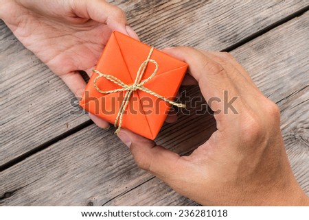 Hand Giving Orange Gift Box and Yellow Ribbon on Wood Background