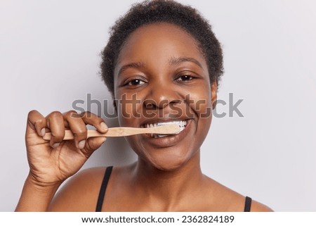 Horizontal shot of dark skinned woman with curly hair makes dental care wants to have healthy teeth focused at camera fight against caries in morning routine isolated on white background. Oral hygiene