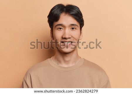 Portrait of handsome dark haired man smiles positively dressed in casual t shirt being satisfied with good news wears casual t shirt isolated over brown background. People and emotions concept