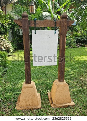 BLANK HANGING GARDEN SIGN ON WOODEN POSTS - Empty decorative wood signage board free standing ready for your own text writing, outdoors with a leafy garden background and green lawn
