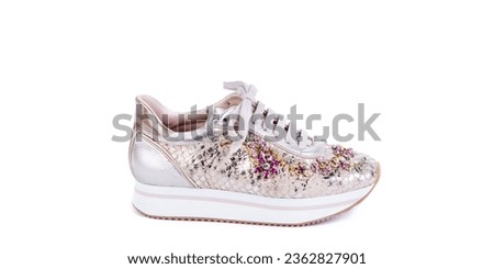 Bold woman's shoe made from pink material, imitating fish scales, with a white ribbed sole decorated with a multi-colored rhinestone floral ornament on a white background. Fashion photography.