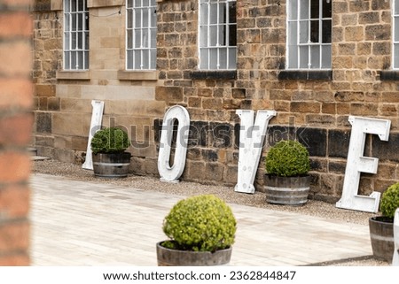 Wooden love letters in white outside wedding venue stone walls and windows in courtyard for marriage ceremony.