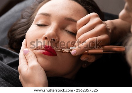 Young woman making lips tatouage in a dressing makeup room. Lips tatouage process .Woman making lips blushing. Make-up artist in beauty studio doing makeup for beautiful girl. Making mua. Royalty-Free Stock Photo #2362857525