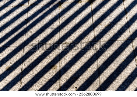 A full frame abstract photograph of shadows from a fence on a concrete pavement