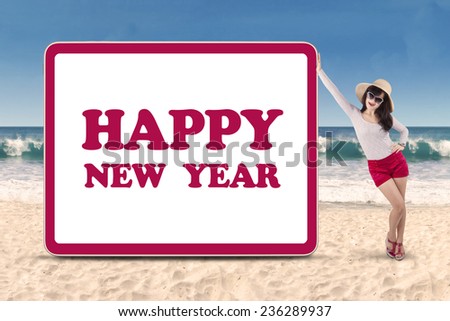 Young woman standing next to the new year billboard on beach