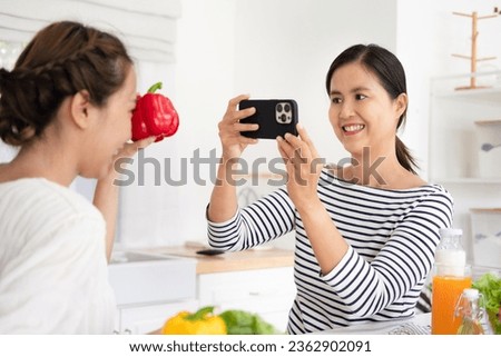 Happy two woman friends shooting video with mobile phone to share online while cooking in kitchen at home