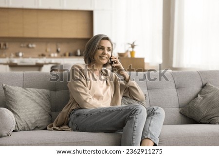 Happy middle aged woman making telephone call from home, talking on mobile phone, enjoying leisure, cellphone conversation, communication, resting on sofa, smiling, laughing