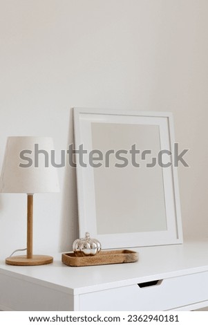 Vertical blank frame mockup with a modern lamp and wooden tray with a silver decorative pumpkin. Minimalistic interior design, home, office desktop.