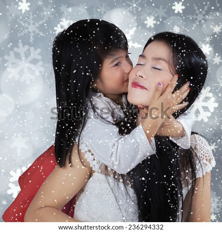 Cute little girl kiss her mother from the back in snowy day against light glitter background