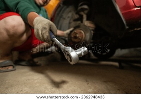 A man repairing a car in a garage holds a ratchet wrench in the cell. A man takes a ratchet wrench to remove rusty bolts from a car wheel hub. Car repair in the garage. Royalty-Free Stock Photo #2362948433