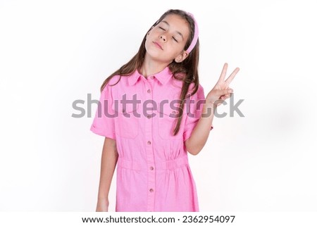 Beautiful kid girl wearing pink dress over white background smiling with happy face winking at the camera doing victory sign. Number two.