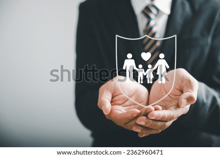 Supporting family futures, Businessman protective gesture complements young family silhouette. Health and house insurance icons symbolize protection, reinforcing family life insurance. Royalty-Free Stock Photo #2362960471