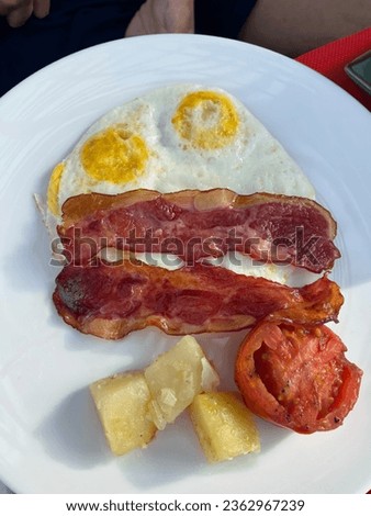 An image of an American breakfast set consisting of bacon, two sunny side up eggs, grilled tomatoes on a white plate