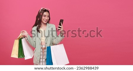 Trendy beautiful young Asian teen woman carrying colorful paper bags shopping online with mobile phone isolated on pink banner background with copy space Royalty-Free Stock Photo #2362988439