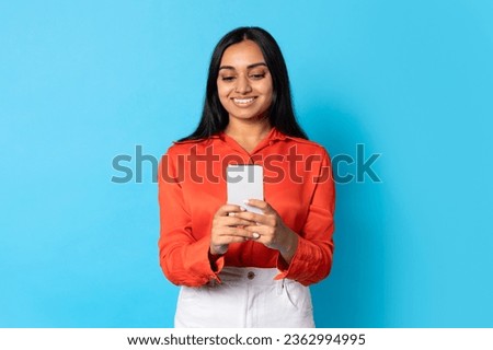 Nice Mobile Application. Smiling Young Indian Woman Using Smartphone, Websurfing And Messaging In Studio, Standing Over Blue Background. Phone User Lady Texting, Scrolling Social Media On Gadget Royalty-Free Stock Photo #2362994995