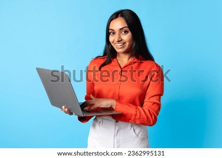 Indian Woman Using Laptop Computer, Typing And Smiling To Camera While Learning Online On Blue Studio Background, Smiling To Camera. Freelancer Lady Websurfing And Working On PC Royalty-Free Stock Photo #2362995131