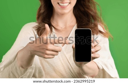 Happy young european lady point finger at smartphone with blank screen, isolated on green studio background, close up. Recommendation sale, website and app for shopping, ad and offer