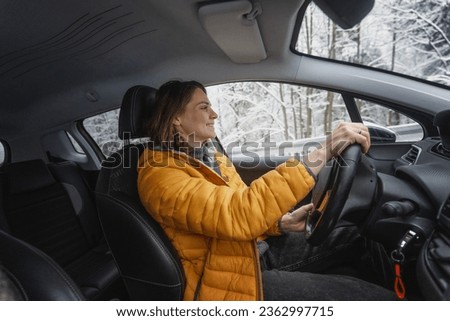 Young happy caucasian woman driving car in winter weather in forest, portrait Royalty-Free Stock Photo #2362997715