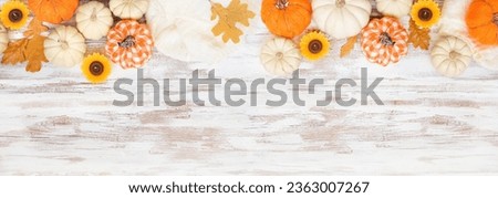 Autumn country farmhouse top border over a white wood banner background. Orange and white cloth pumpkins, sweater, candles and fall leaves. Above view with copy space.