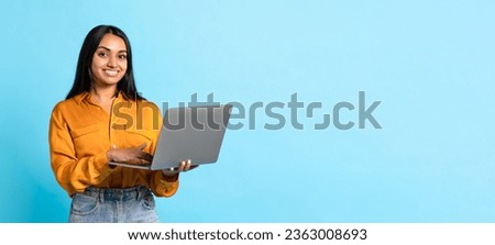 Smiling Middle Eastern Young Woman Posing With Laptop Computer, Websurfing And Working Online Over Blue Background. Studio Shot Of Modern Indian Lady In Casual With PC. Panorama, Copy Space